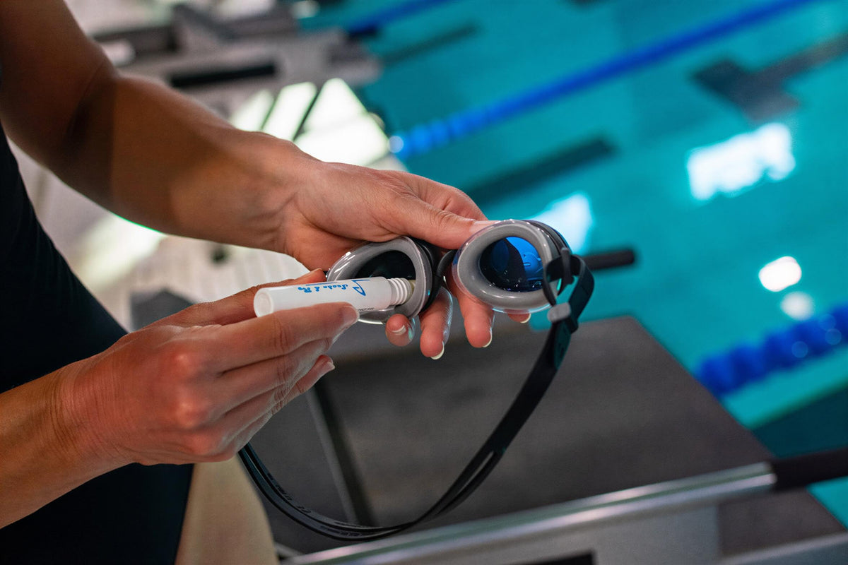 Person applies diluted baby shampoo using the DIY antifog tube to defog swim goggles in a pool setting